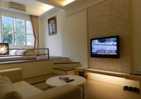 A hotel room with a bed, a TV mounted on the wall, a window with curtains, and a small seating area with a table.
