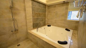 A modern bathroom with a large bathtub, a shower area, and a window providing natural light.