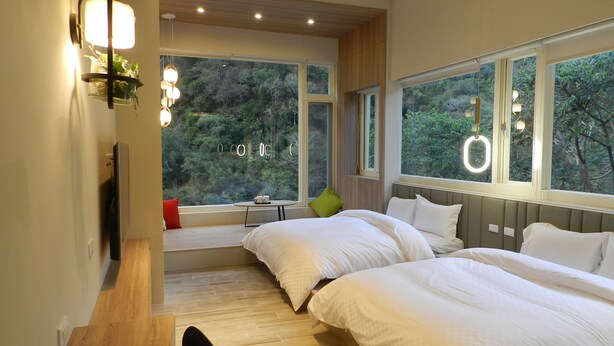 Ein modernes Schlafzimmer mit zwei Betten, großen Fenstern und Blick ins Grüne.
