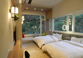 A modern bedroom with two beds, large windows, and a view of greenery.