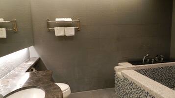 Un baño con lavamanos de mármol, inodoro, bañera con mosaicos y un perchero con dos toallas.