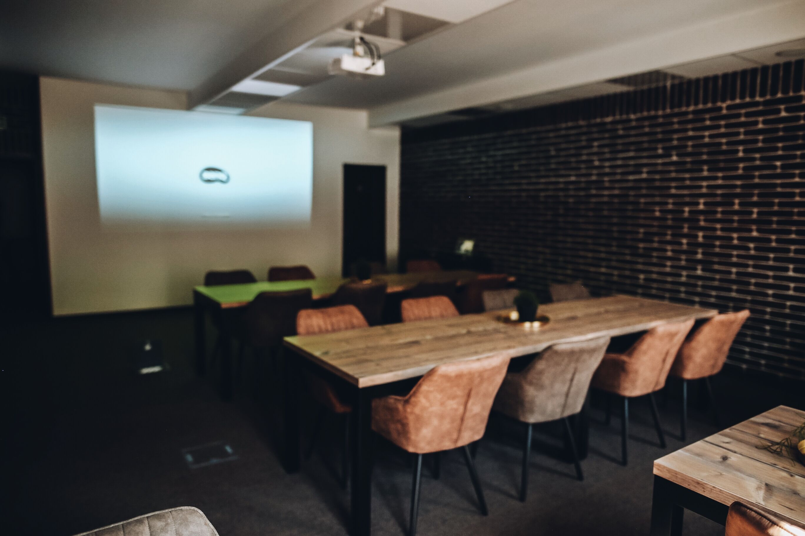 A conference room with a projector screen, wooden tables, and leather chairs.