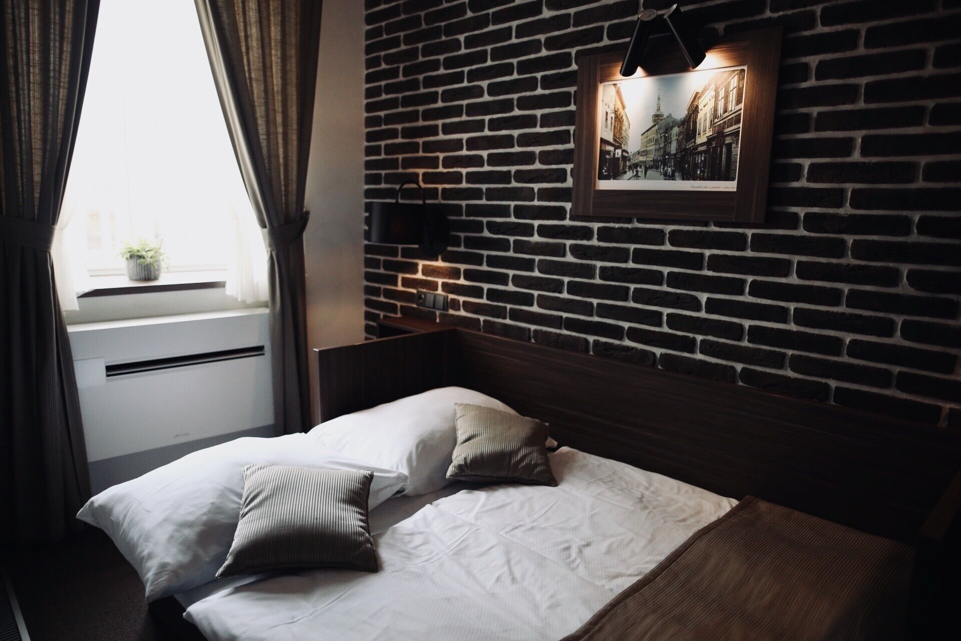 Ein Hotelzimmer mit Backsteinwand, einem Bett mit weißer Bettwäsche und einem gerahmten Bild an der Wand.