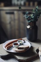 Un plato con salchichas, pan y salsas sobre una tabla de madera.
