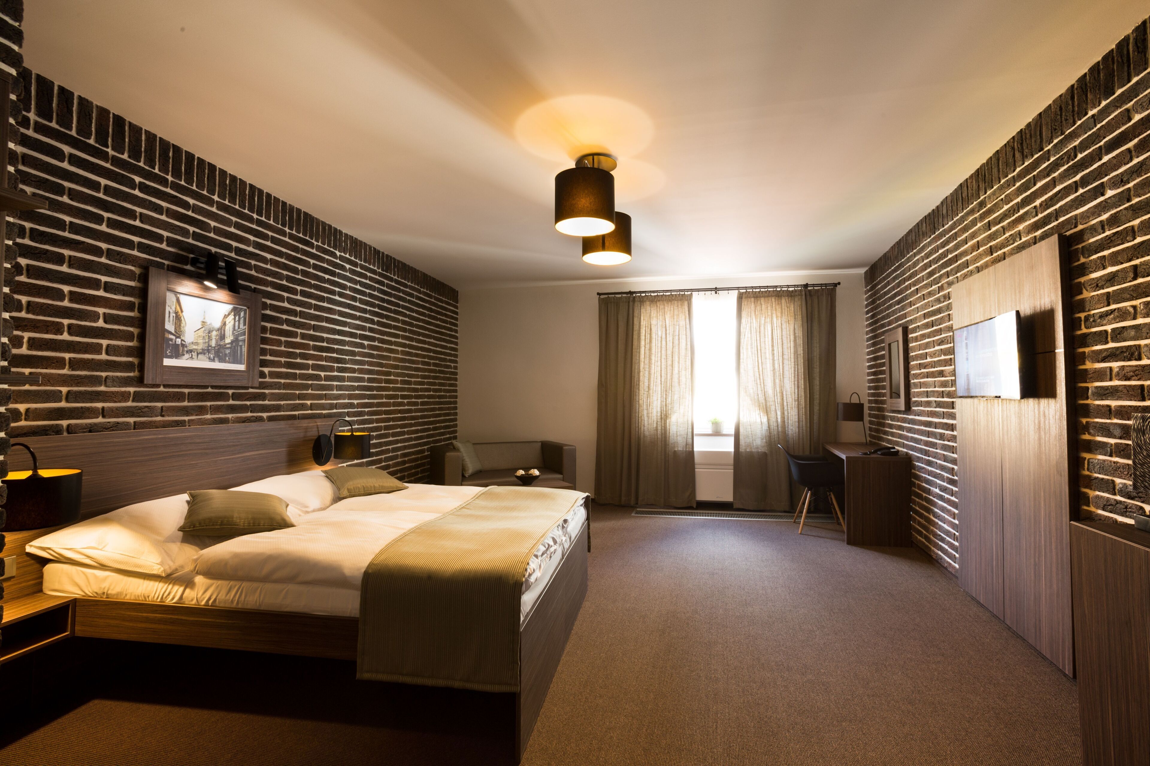 A modern hotel room with a brick wall, a bed, a desk, and a large window with curtains.