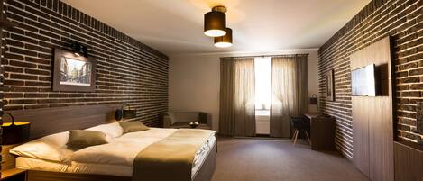 Una habitación de hotel moderna con pared de ladrillo, cama, escritorio y un ventanal con cortinas.