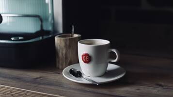 A white cup with a red logo on a wooden table, accompanied by a spoon and a wooden cup.