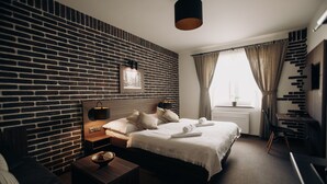 A modern hotel room with a brick-patterned wall, a neatly made bed, a bedside table with a lamp, and a view of the outdoors through a window. - Penzion U Kubesa (Kromeriz)