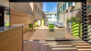 An outdoor patio with wooden flooring, green chairs, a sofa, and potted plants. - Hotel Doria (Genoa)