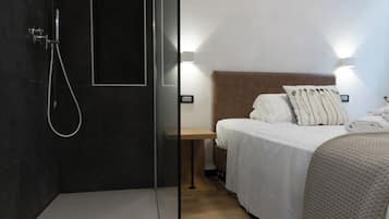 A modern hotel room with a shower, a bedside table, a bed with white bedding, and a headboard.