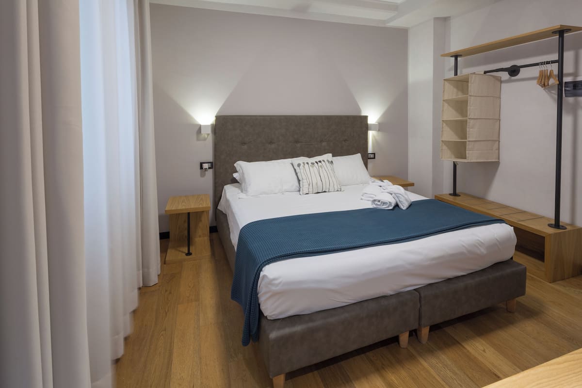 Una habitación de hotel moderna con una cama grande, mesitas de noche, un armario y una estantería empotrada.