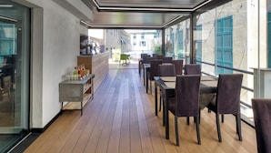 A modern outdoor seating area with wooden flooring, tables, and chairs. - Hotel Doria (Genoa)