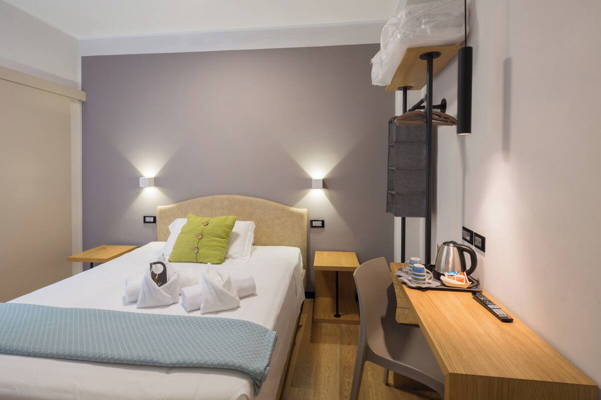 Habitación de hotel con cama, mesitas de noche, escritorio, una silla y una lámpara de pared.
