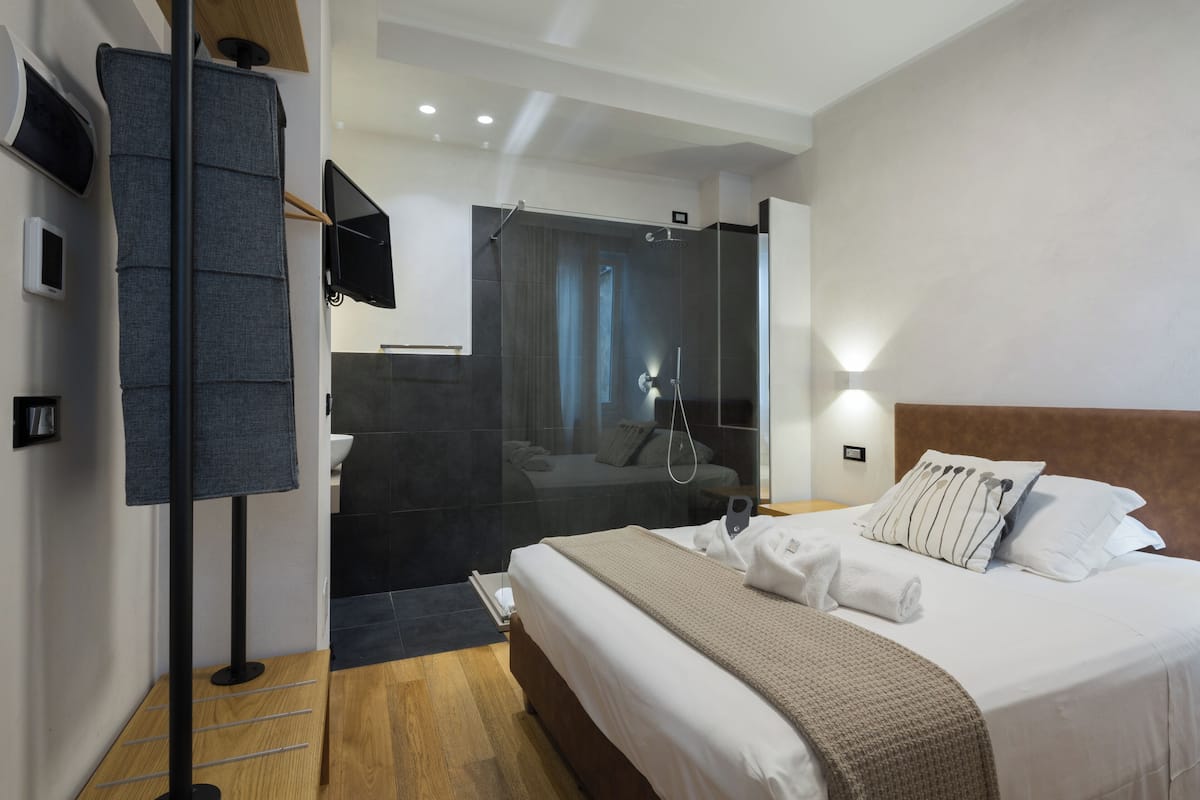 Una habitación de hotel moderna con una cama grande, zona de ducha y televisor de pantalla plana.