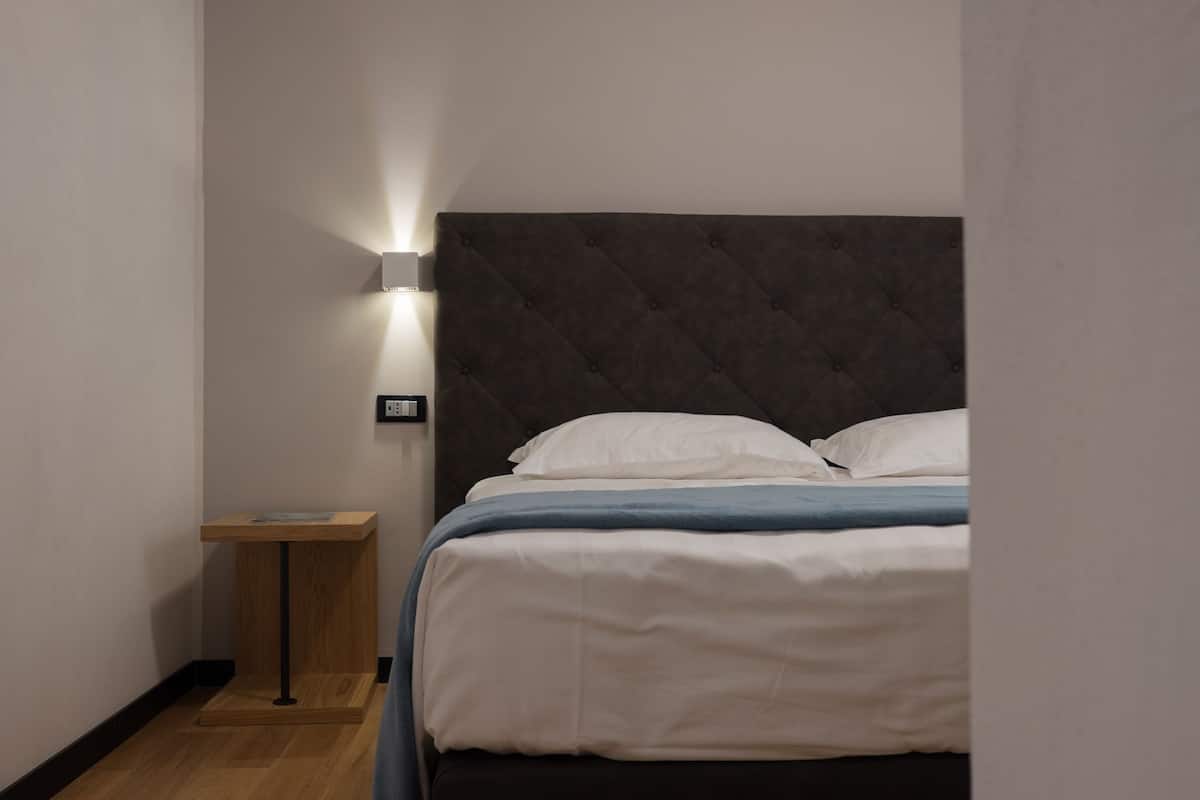 Un dormitorio con cama, mesita de noche, luz empotrada en la pared y toma de corriente.