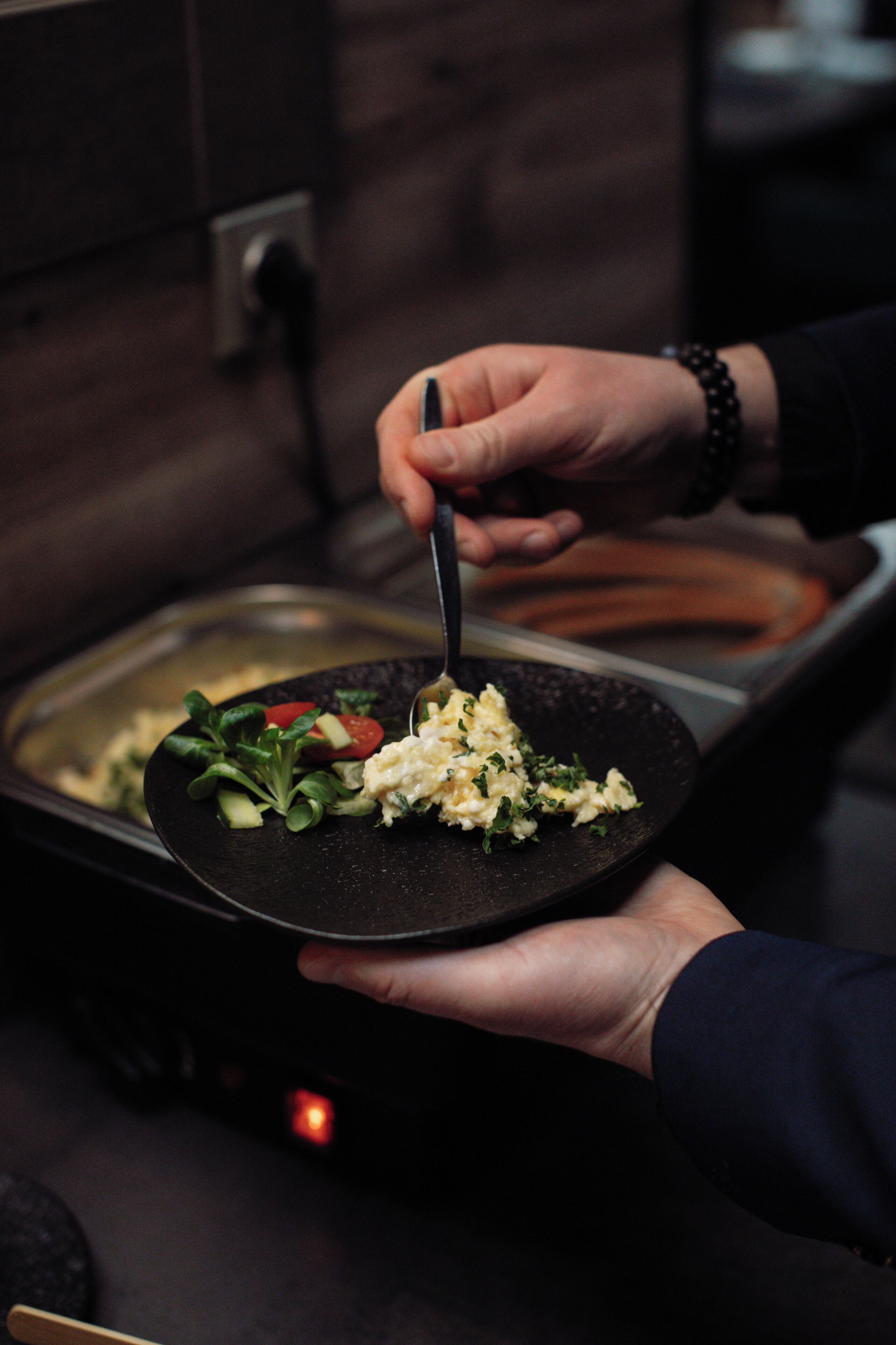 A person holding a plate with scrambled eggs and greens.