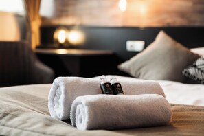 A neatly made bed with rolled towels and two bottles of toiletries.