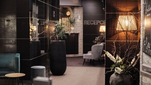 A reception area with a modern design, featuring a reception desk, seating area, and a decorative vase with branches. - Interhotel Tatra (Koprivnice)