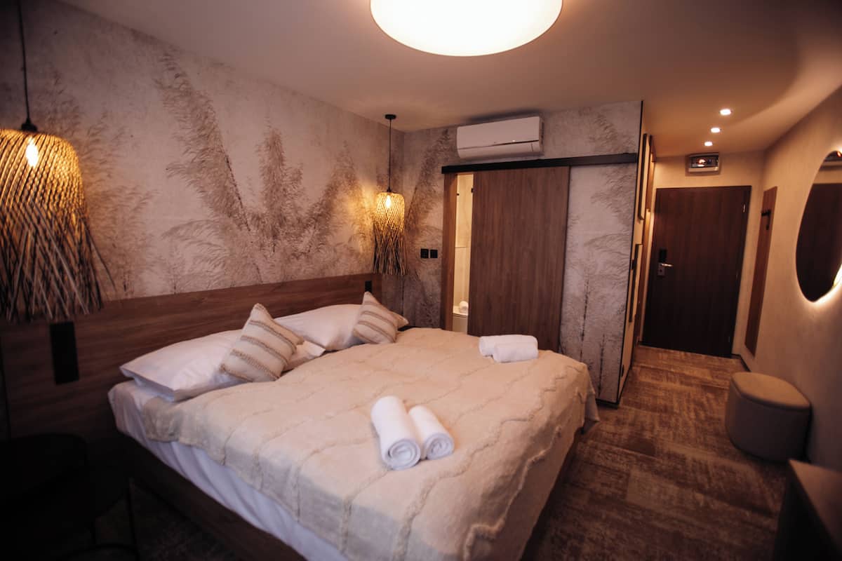 A neatly made bed with a headboard, a wall-mounted air conditioner, and a hanging light fixture.