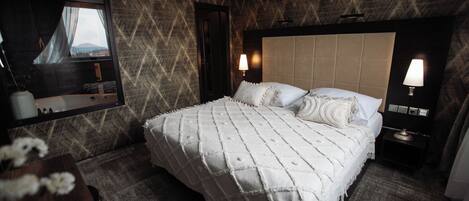 A hotel room with a large bed, a mirror, two bedside lamps, and a view of the outdoors through the window.