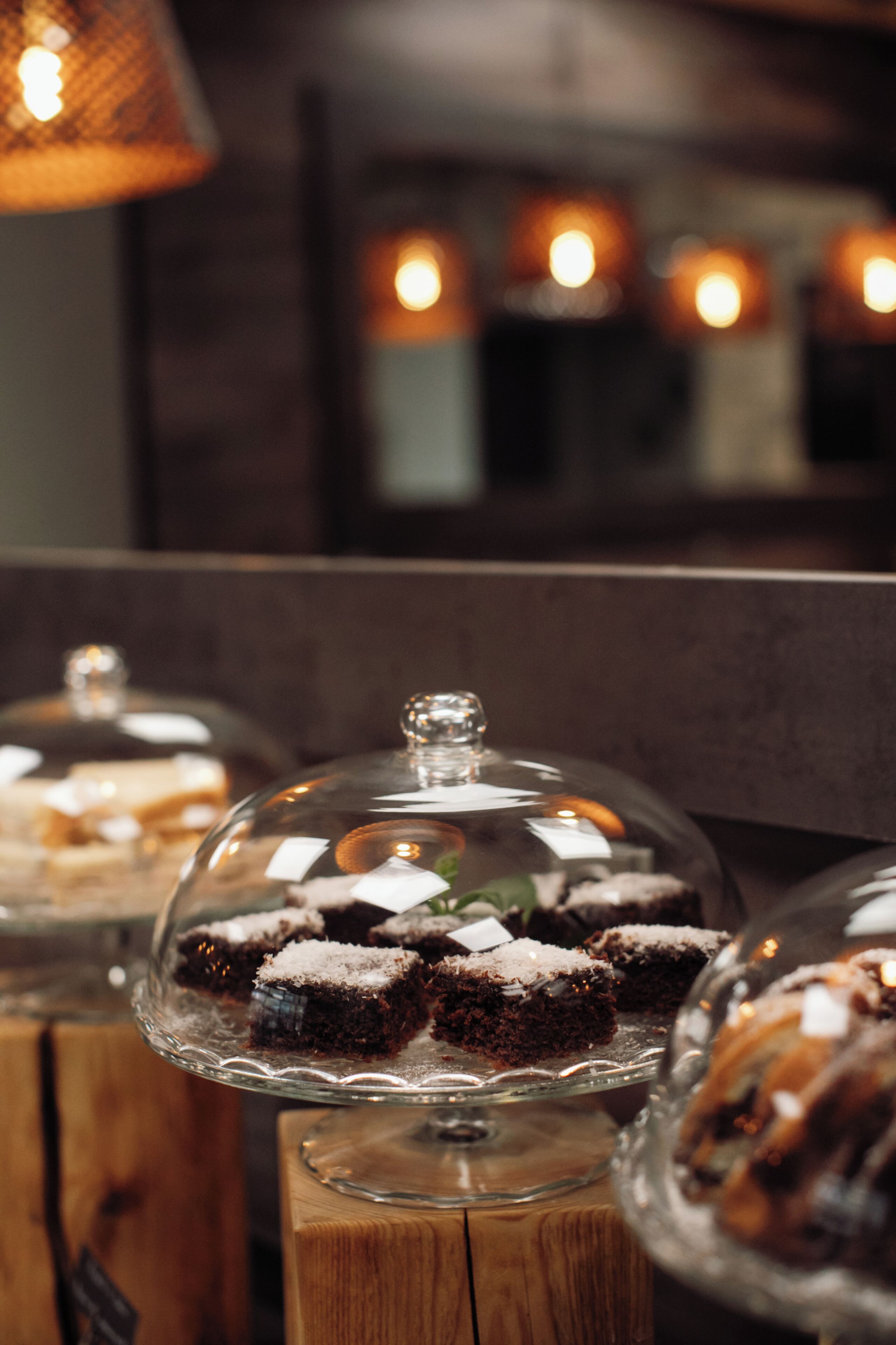 A dessert display with cakes under glass domes on wooden stands.