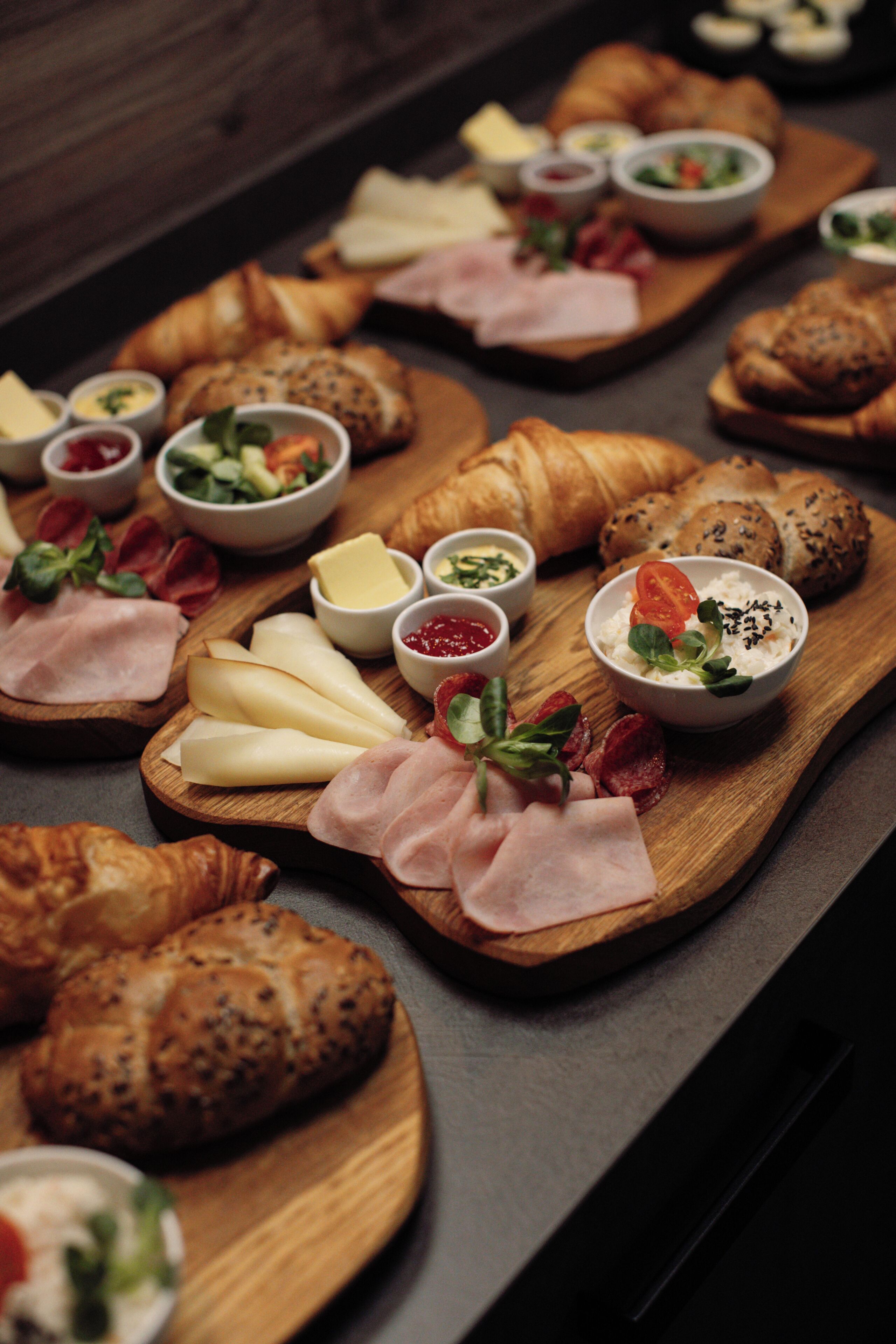 A wooden board with various cheeses, meats, and pastries.