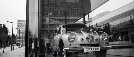 A vintage car with a license plate 'TATRA 87' parked in front of a modern building with a glass facade.