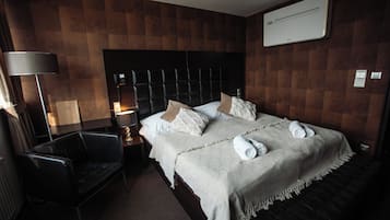 A hotel room with a large bed, a bedside table with a lamp, a chair, and a wall-mounted air conditioner.