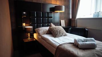 Habitación de hotel con diseño moderno, que incluye una cama grande con cabecera, una mesita de noche con lámpara y vistas al exterior a través de una ventana.