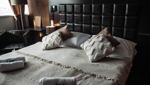 A hotel room with a large bed, a headboard with a textured design, a bedside table with a lamp, and a chair. - Interhotel Tatra (Koprivnice)