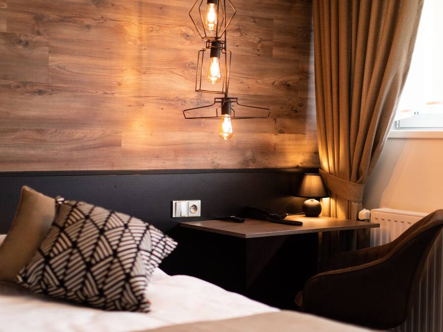 Ein Hotelzimmer mit einer Holzwand, einem Bett mit gemusterten Kissen, einem Nachttisch mit Lampe und einem Sessel.