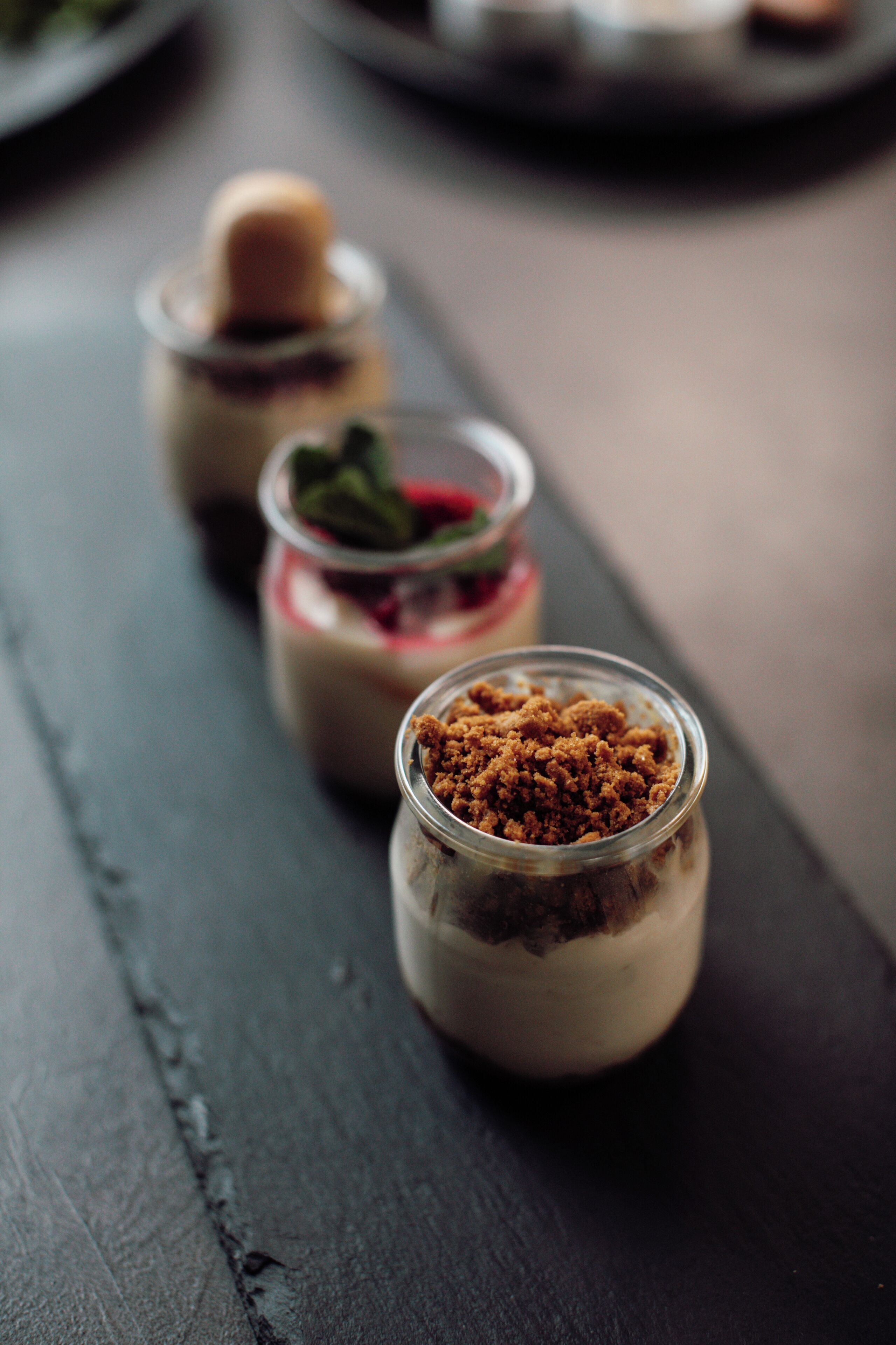 Trois petits pots de dessert sur une surface en bois foncé.