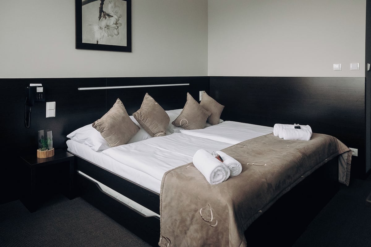 A neatly made bed with a brown blanket, a white pillow, and a rolled towel on the side.