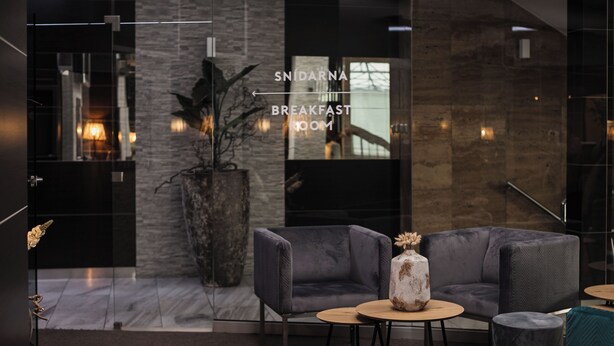 A modern lounge area with a grey sofa, a coffee table, and a potted plant. A sign indicates the direction to the breakfast room. - Interhotel Tatra (Koprivnice)