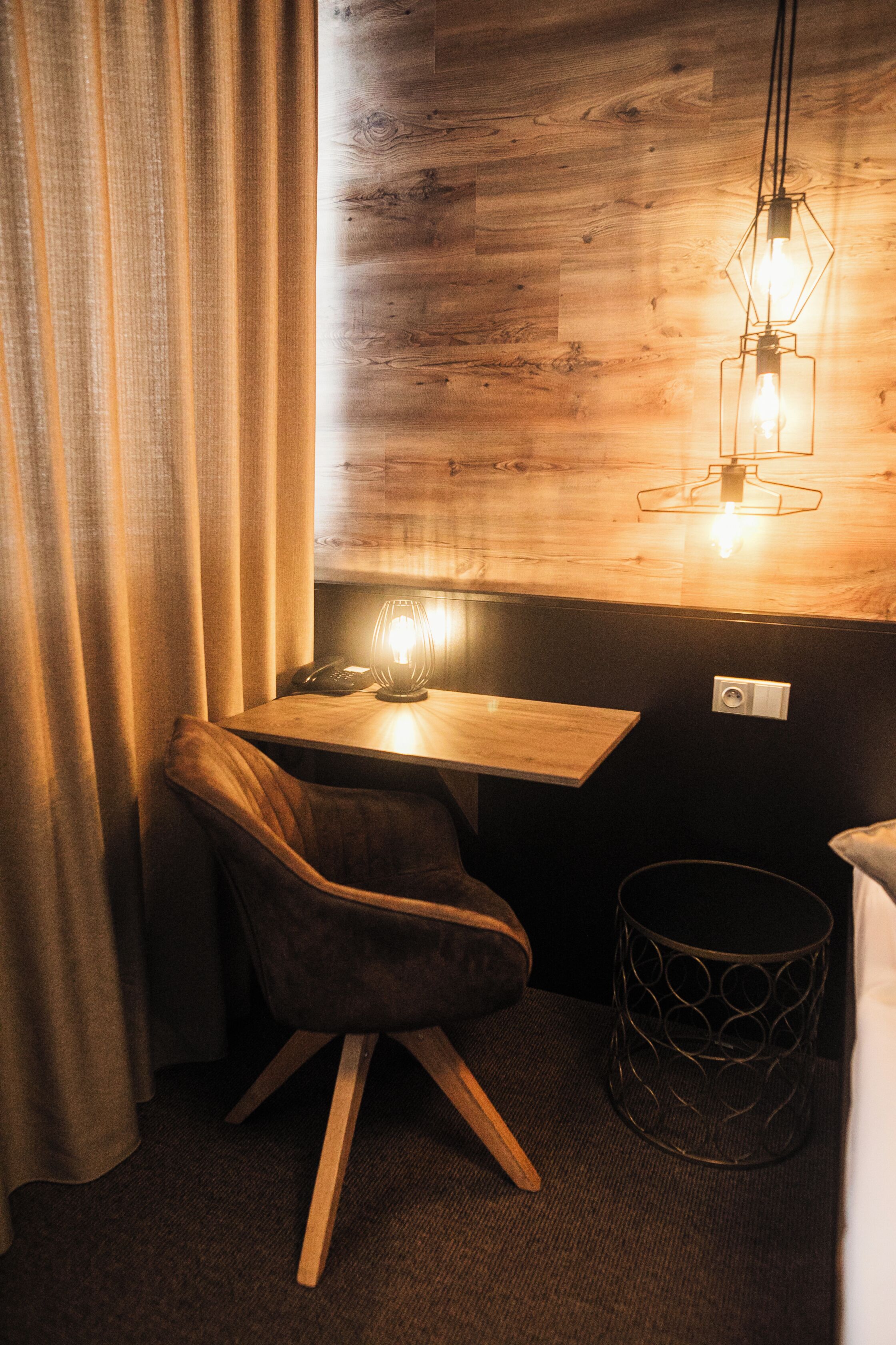 Une petite pièce agréable, dotée d’un bureau en bois, d’une chaise, d’une lampe et d’un téléphone.
