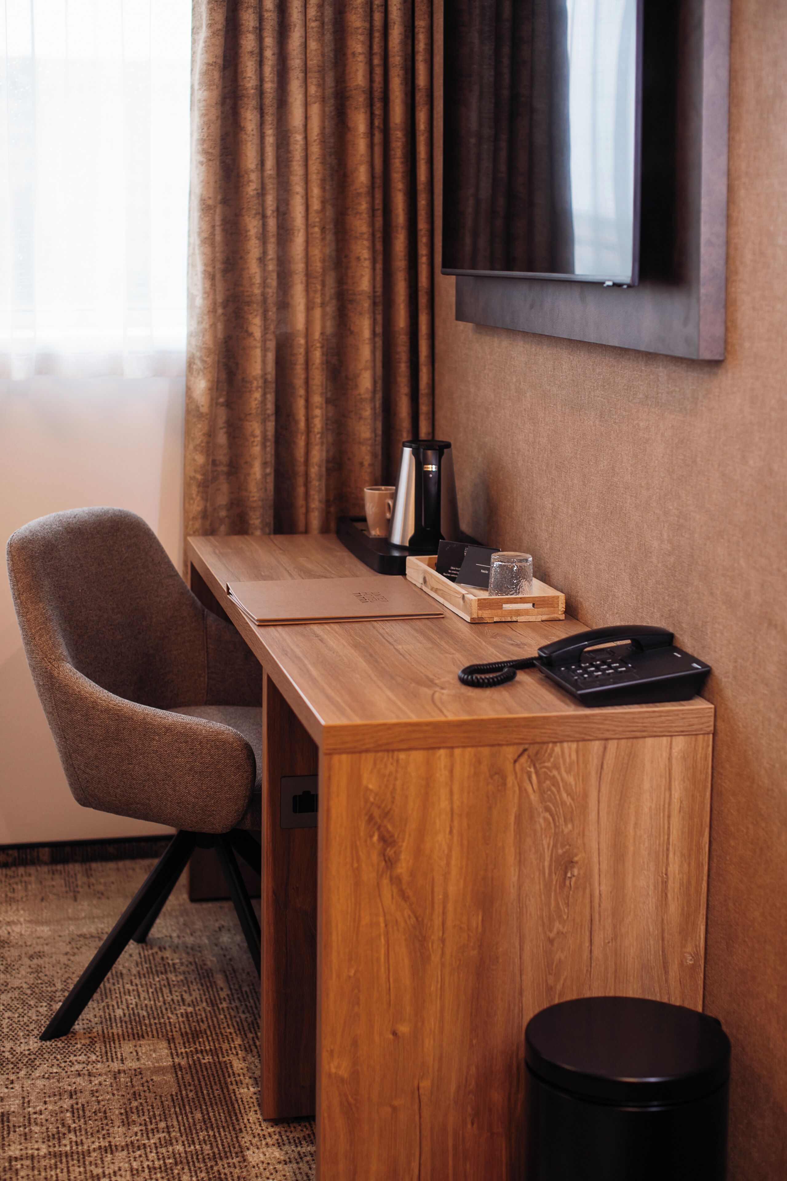 A hotel room with a wooden desk, a chair, a telephone, a small tray with items, and a TV mounted on the wall.