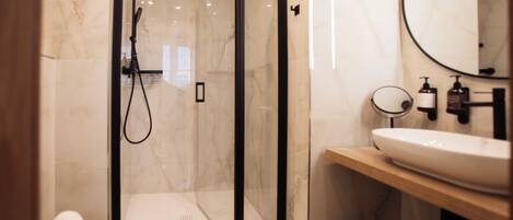 A modern bathroom with a glass-enclosed shower, a white toilet, a wooden vanity with a large mirror, and a white sink.