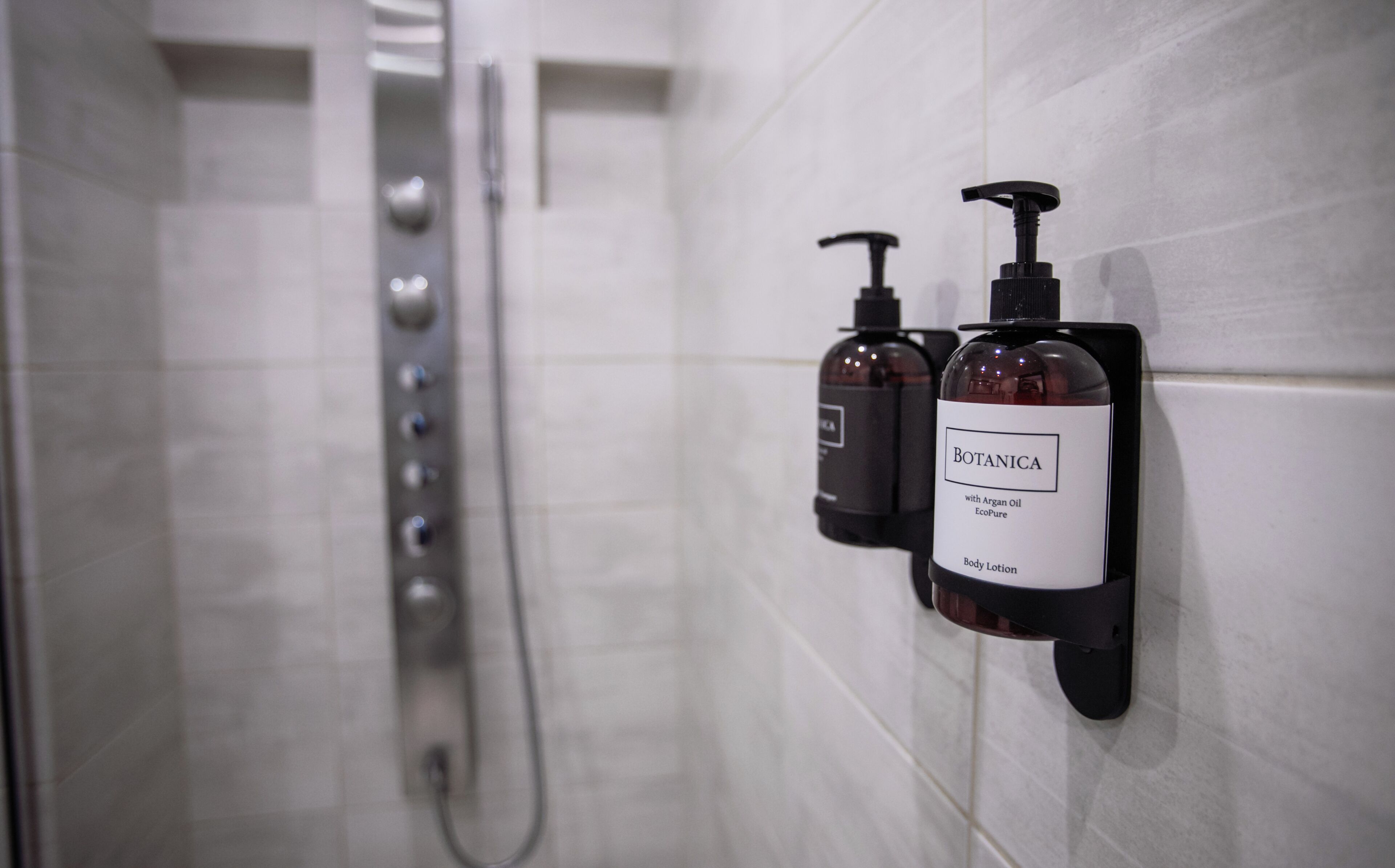 A bathroom with a shower and two body lotion dispensers labeled 'BOTANICA with Argan Oil EcoPure Body Lotion'.