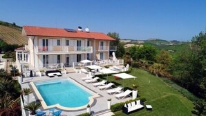 A large building with a swimming pool, sun loungers, and a well-maintained lawn.