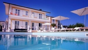 A two-story building with a swimming pool, outdoor seating, and umbrellas.