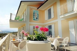 A hotel balcony with outdoor seating, a potted plant, and a painting on the wall.