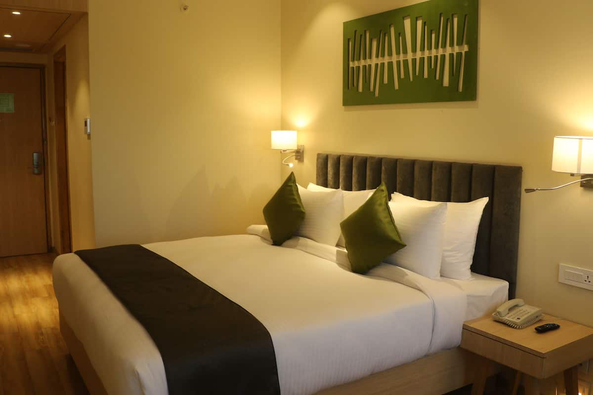 A hotel room with a bed, bedside lamps, a telephone, and a green abstract painting on the wall.