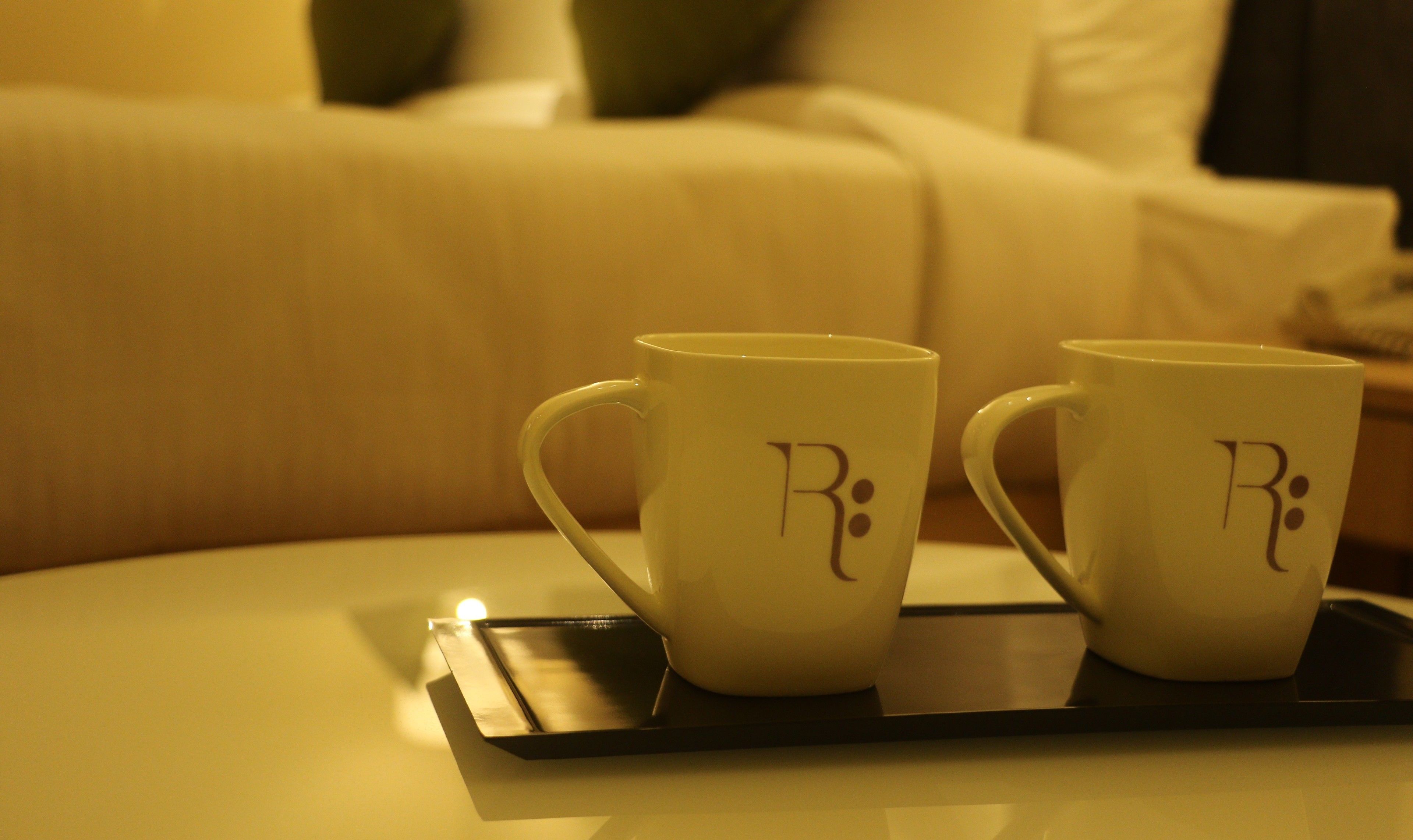 Two white mugs with a logo on a tray.