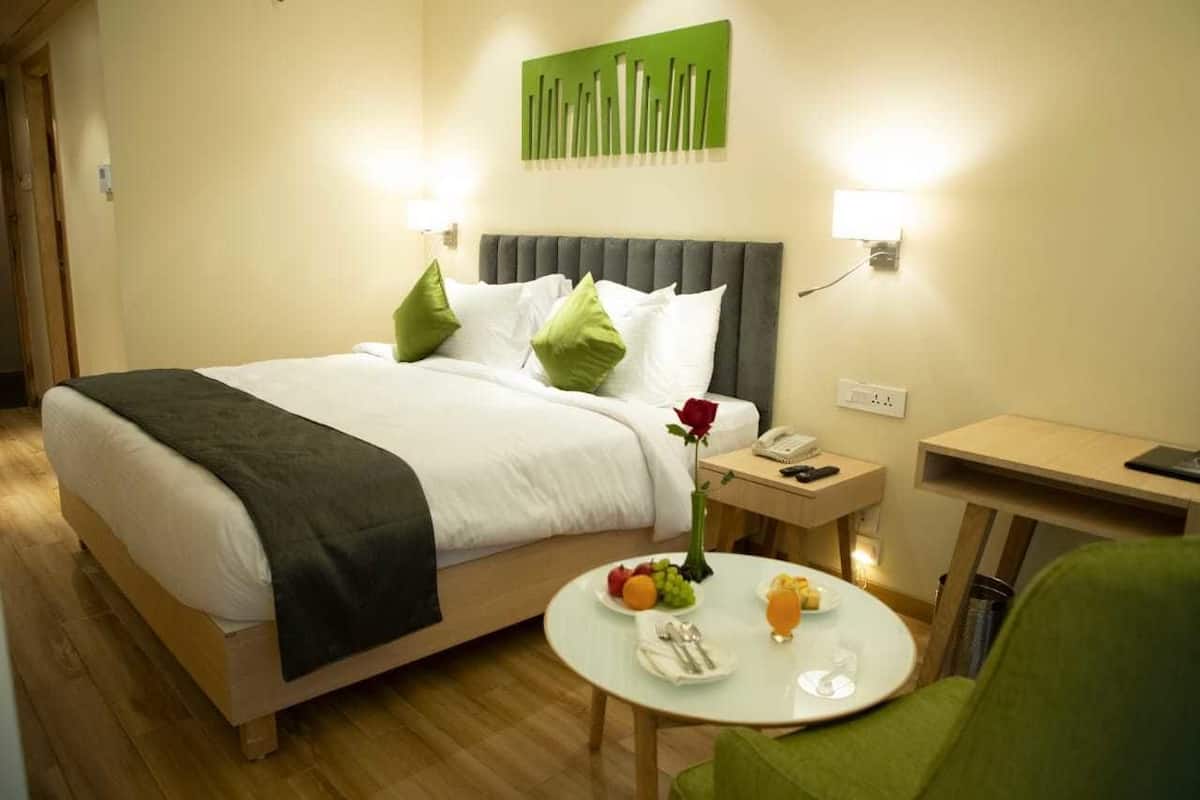 A hotel room with a bed, bedside table, and a small round table with breakfast items.