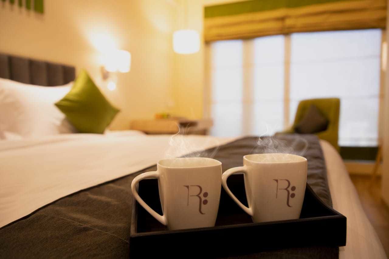 A hotel room with a bed, pillows, and a tray with two mugs.