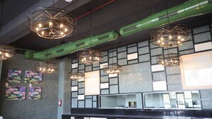 A modern interior with geometric wall patterns, multiple hanging circular chandeliers, and green ductwork. - Regenta Central Harsha Vapi (Pardi)