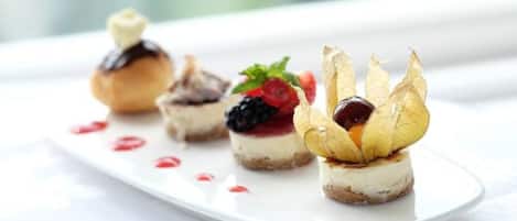 A white plate with four dessert items, each topped with a different fruit and a chocolate drizzle.
