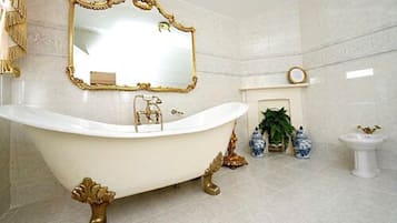 A luxurious bathroom with a freestanding bathtub, a large mirror with an ornate frame, a small fireplace, and decorative vases.