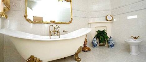 A luxurious bathroom with a freestanding bathtub, a large mirror with an ornate frame, a small fireplace, and decorative vases.