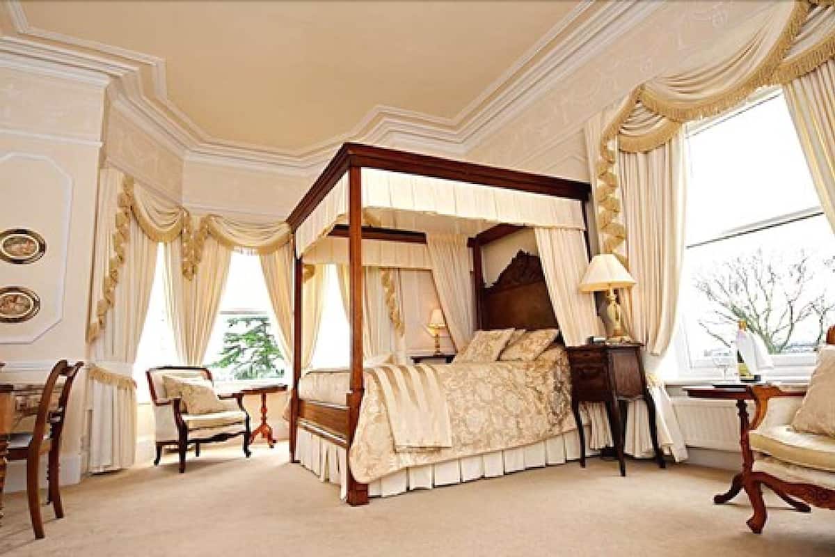 Un lit à baldaquin, un coin salon avec un fauteuil et une table, et une vue sur l’extérieur par une fenêtre.